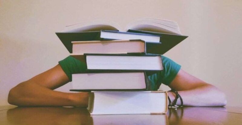 Person sitting behind a stack of books on a table
