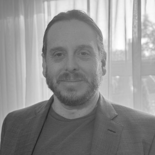 Acquisitions editor Eli is a fair-skinned male with facial hair and his hair pulled back. He wears a blazer over a dark t-shirt