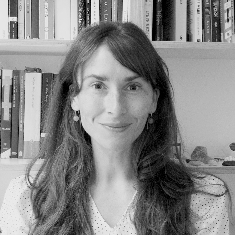 A developmental editor with long brown hair in front of a bookshelf.