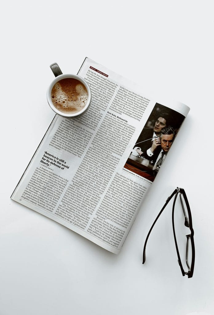 A coffee cup and glasses next to an article by a journalist who might write a book.