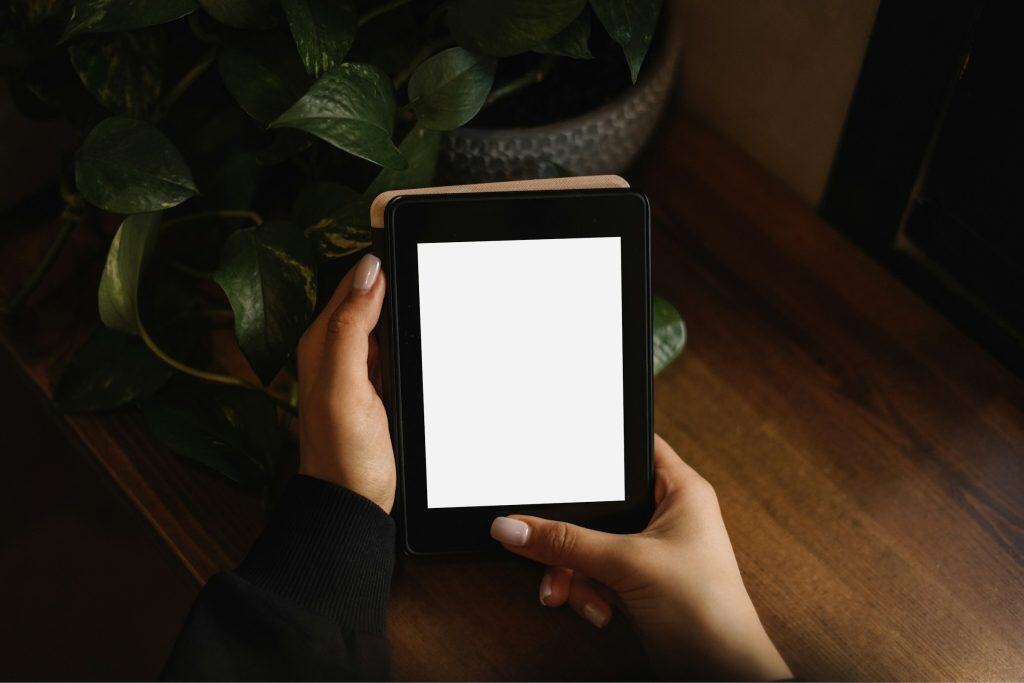 A pair of hands hold a tablet before a plant