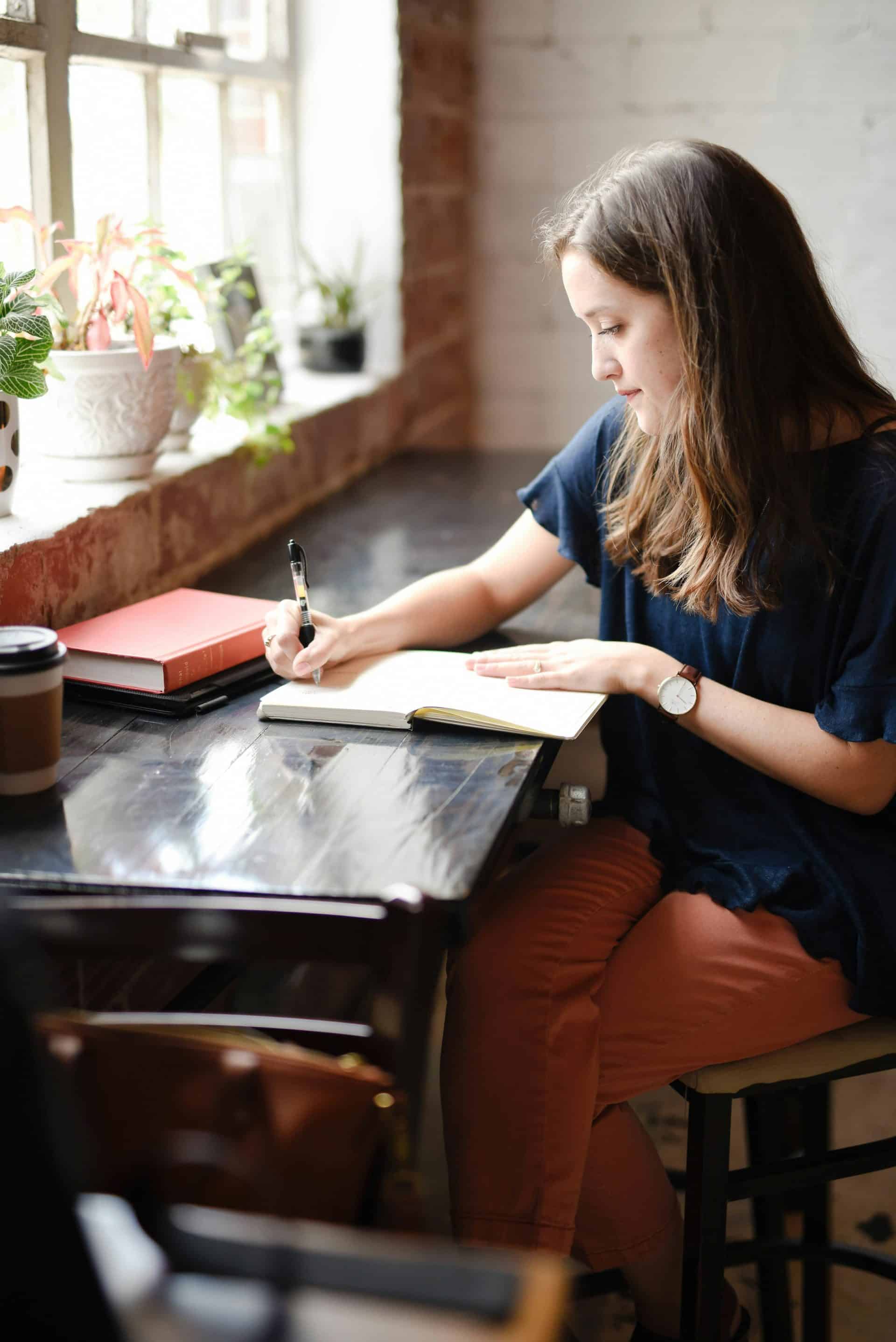 An academic writes at a desk by a window.