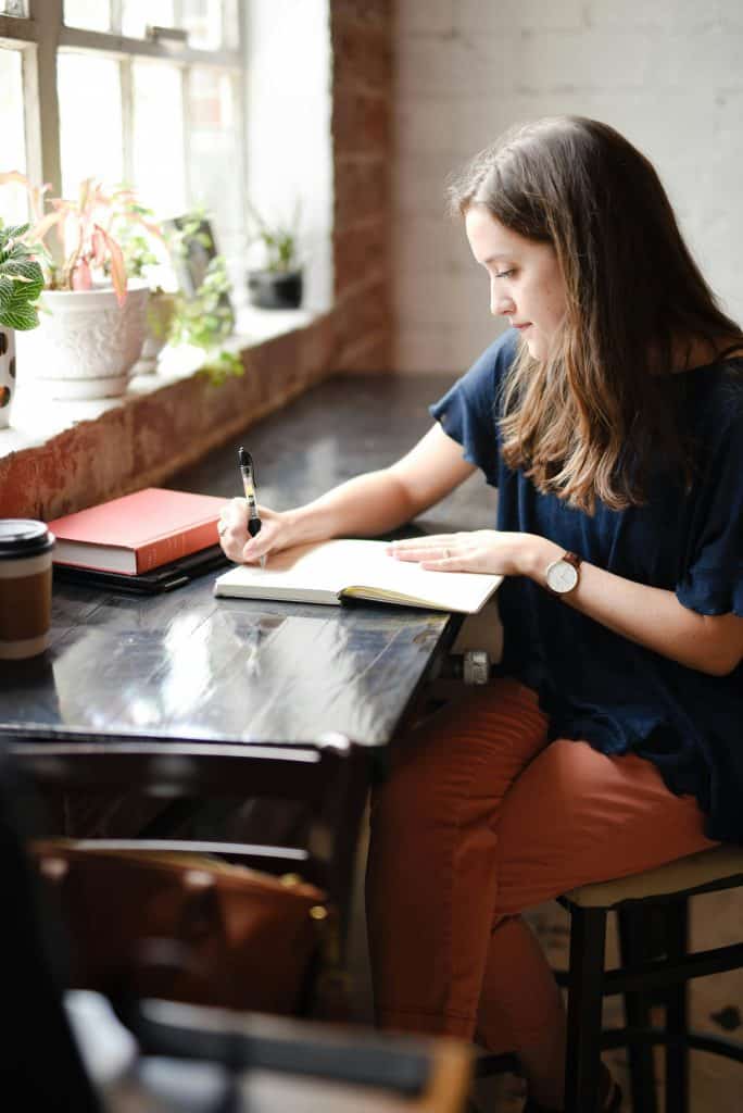 An academic writes at a desk by a window.