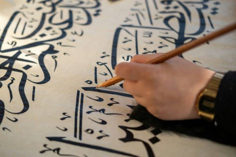 A hand writes Arabic calligraphy.