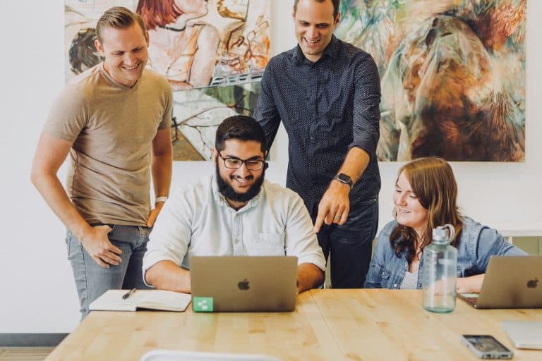 A group of coworkers gathered around a laptop.